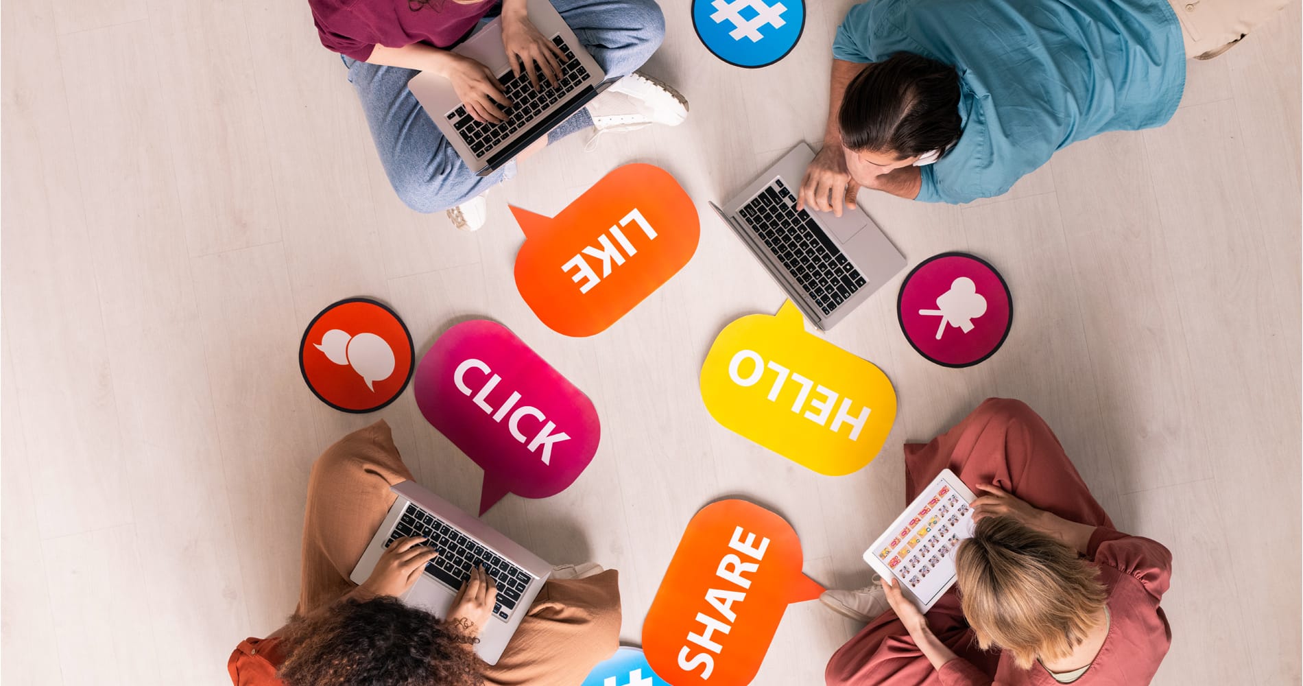 Four friends using mobile gadgets on the floor surrounded by social media related words and icons